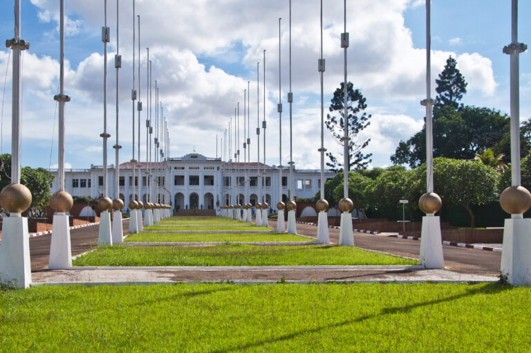 The National Museum of Cameroon, a white building behind a lawn and flagpoles beneath a blue sky.