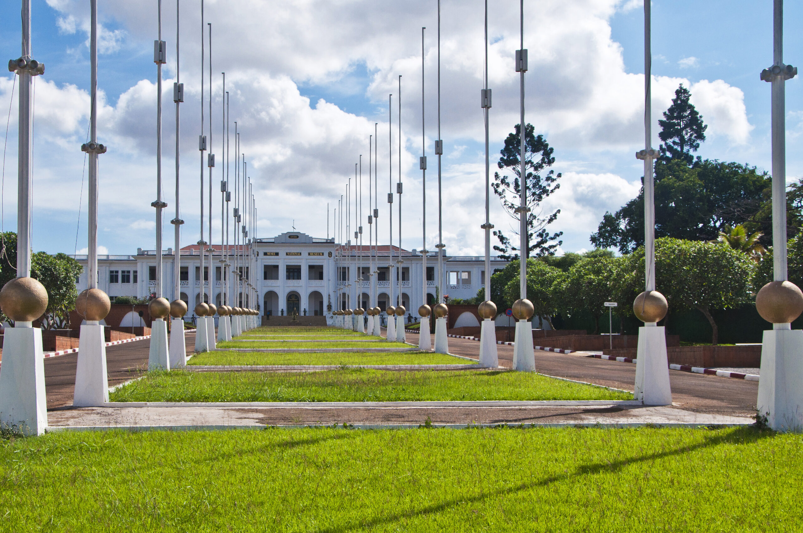 The National Museum of Cameroon, a white building behind a lawn and flagpoles beneath a blue sky.